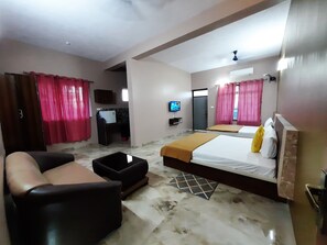 Una habitación de hotel con cama, sofá, televisión y una pequeña cocina.