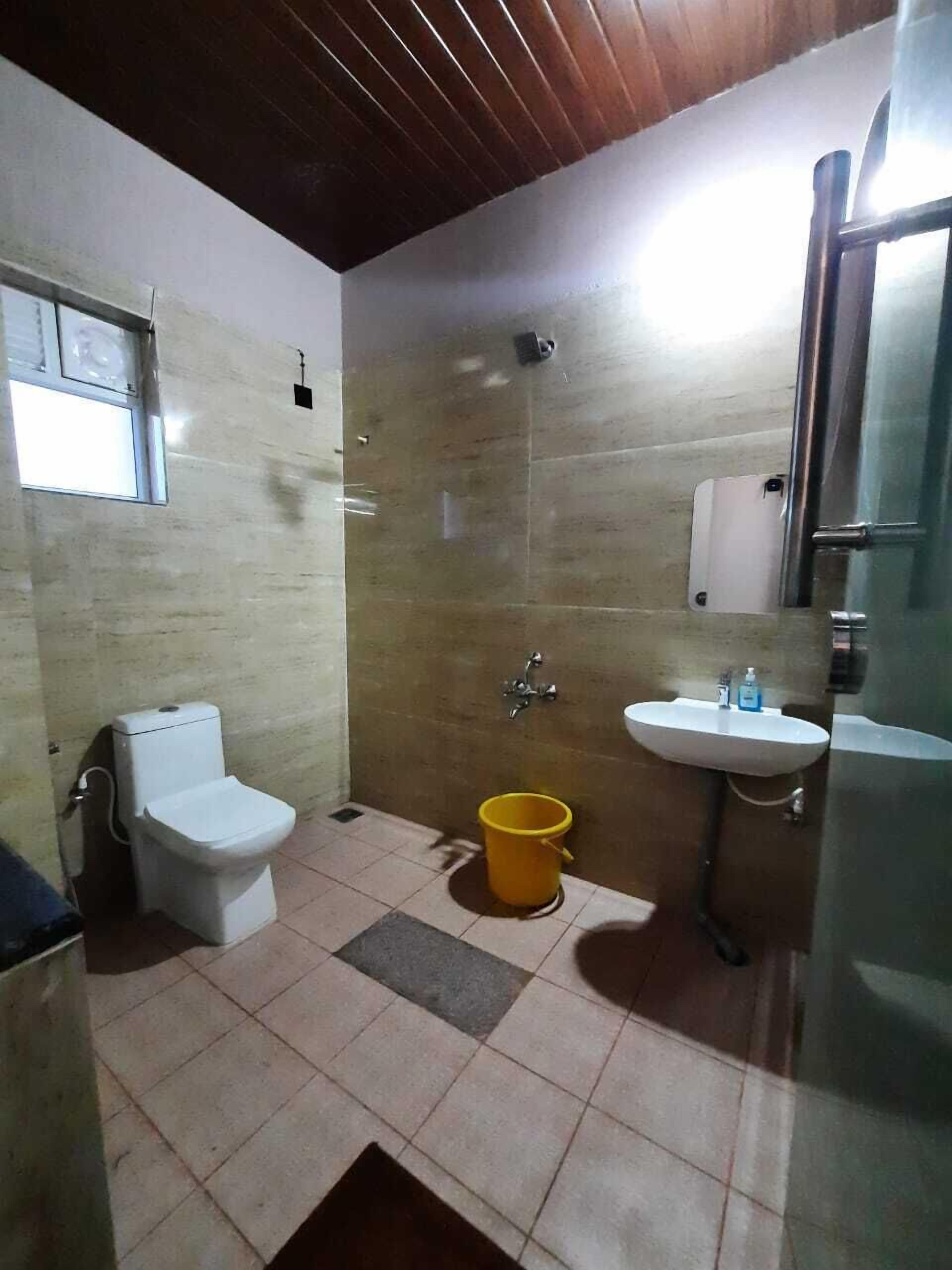 A small bathroom with a toilet, sink, shower, and a yellow bucket on the floor.