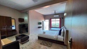 Una habitación amplia con una cama grande, un sofá, una pequeña cocina y un balcón con vistas.
