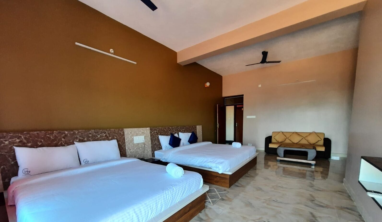 A hotel room with two beds, a sofa, a ceiling fan, and a marble floor.