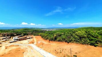 A construction site with a dirt road, buildings, and a forested area under a clear blue sky.