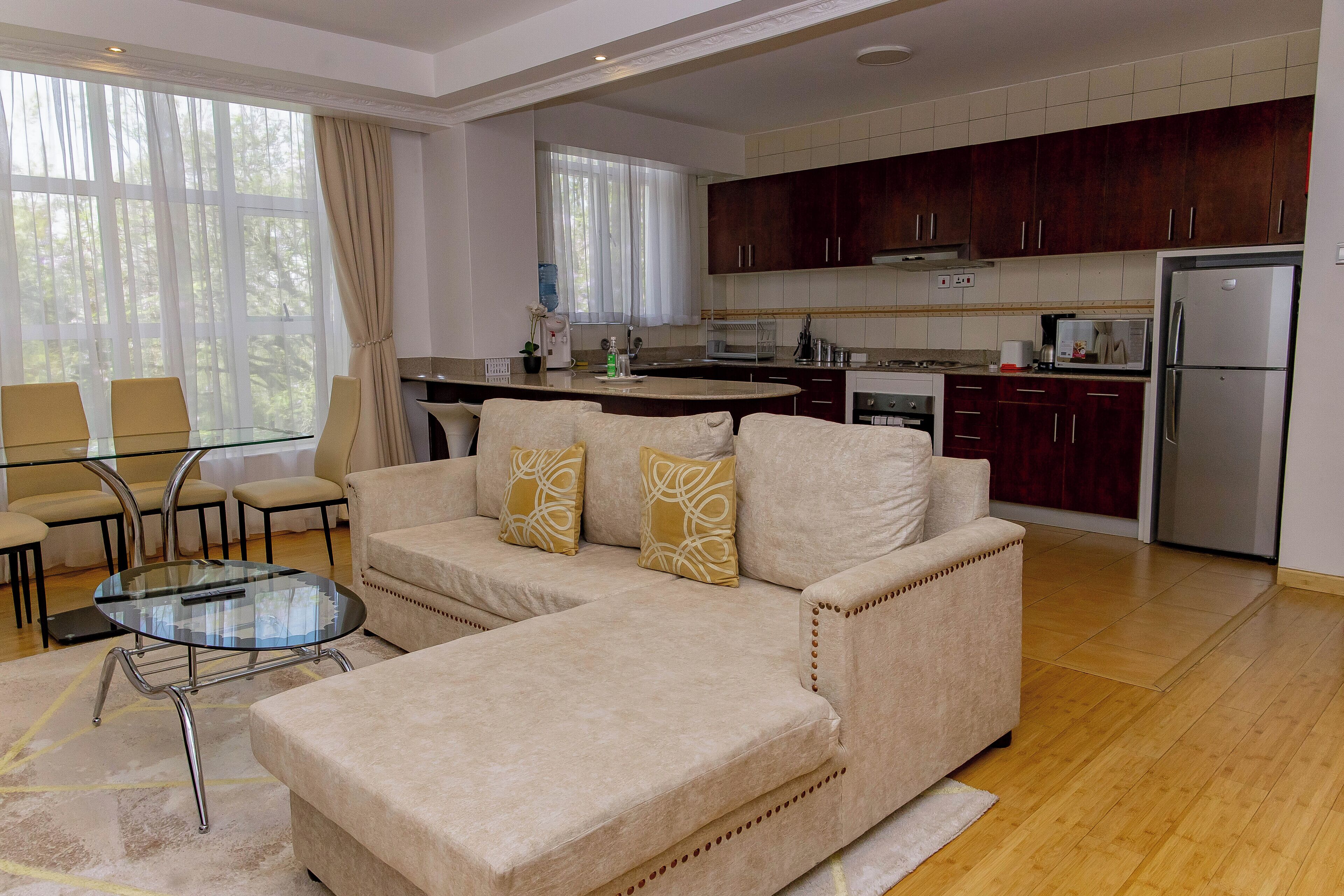 A modern living room with a beige sofa, glass coffee table, and a dining area with chairs.