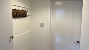 A hallway with a white door, a coat rack with hooks, and a hanging light fixture. - Make yourself at home in the quaint wee village of Rhu. (Rhu)
