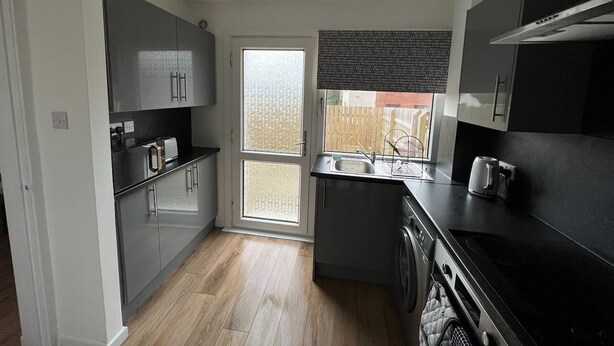 A compact kitchen with stainless steel appliances, a built-in oven, and a window with a view of the outside. - Make yourself at home in the quaint wee village of Rhu. (Rhu)