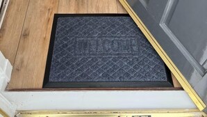 A wooden floor, a gray door with a brass handle, and a black doormat with the word "WELCOME". - Make yourself at home in the quaint wee village of Rhu. (Rhu)
