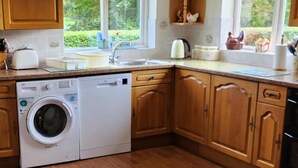 Een keuken met houten kastjes, een ingebouwde vaatwasser, een wasmachine, een gootsteen en een raam met uitzicht op groen.