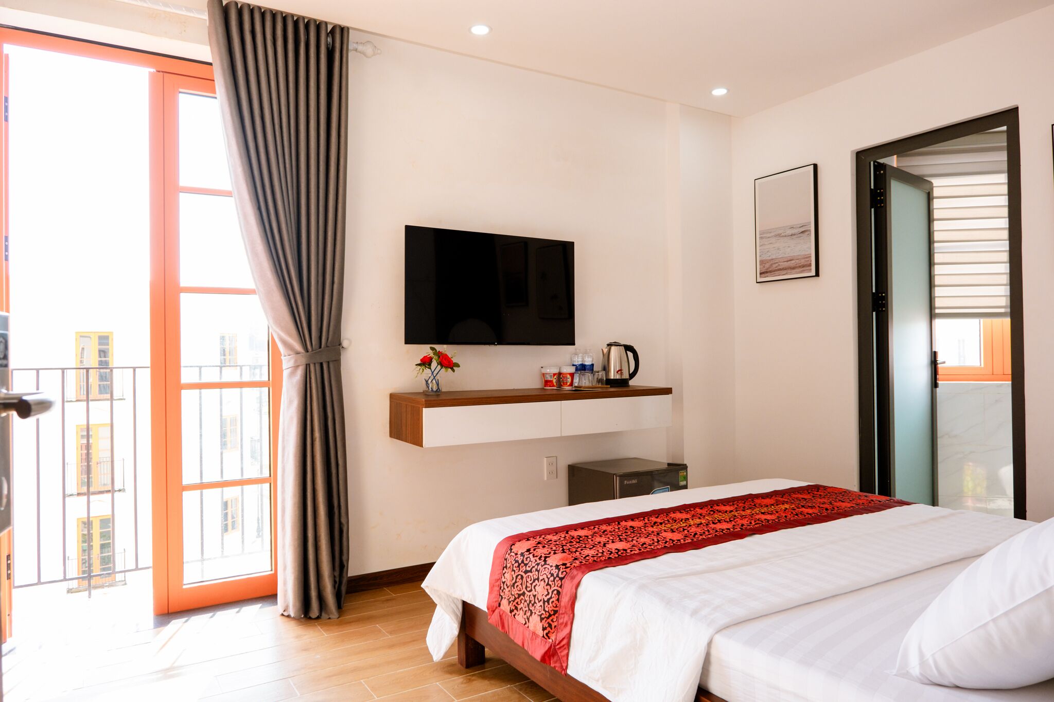 A hotel room with a bed, a TV mounted on the wall, a small coffee maker, and a window with curtains.
