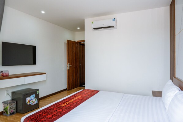 A modern hotel room with a bed, a TV mounted on the wall, a small refrigerator, and an air conditioning unit. - Hoang Long Hotel Phu Quoc (Phu Quoc)