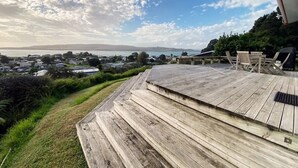 A wooden deck with a view of a coastal town and ocean. - Little Aotea bach with sea views (Kawhia)