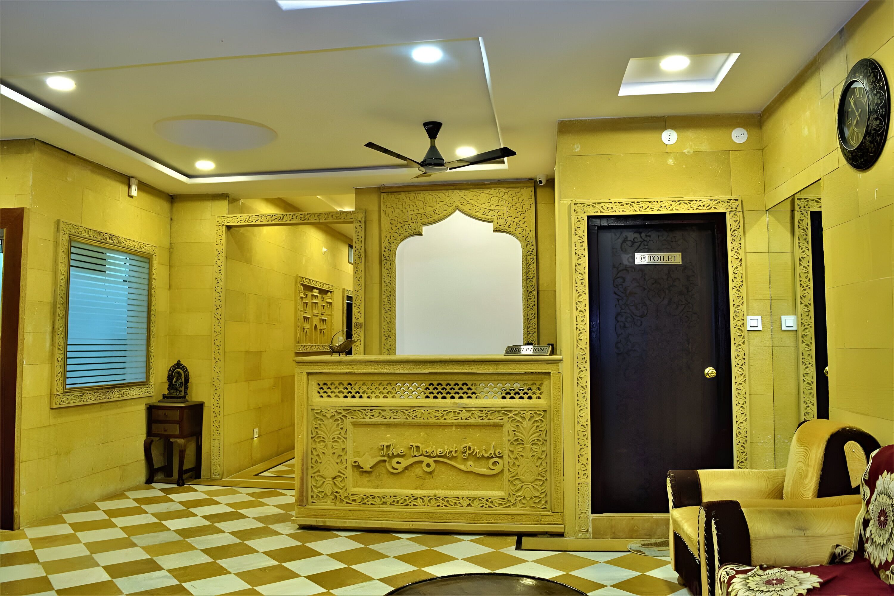 A lobby with a checkered floor, a reception desk, a ceiling fan, and a door labeled "TOILET".