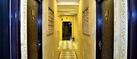 A hotel hallway with ornate doors, a checkered floor, and a central light fixture.