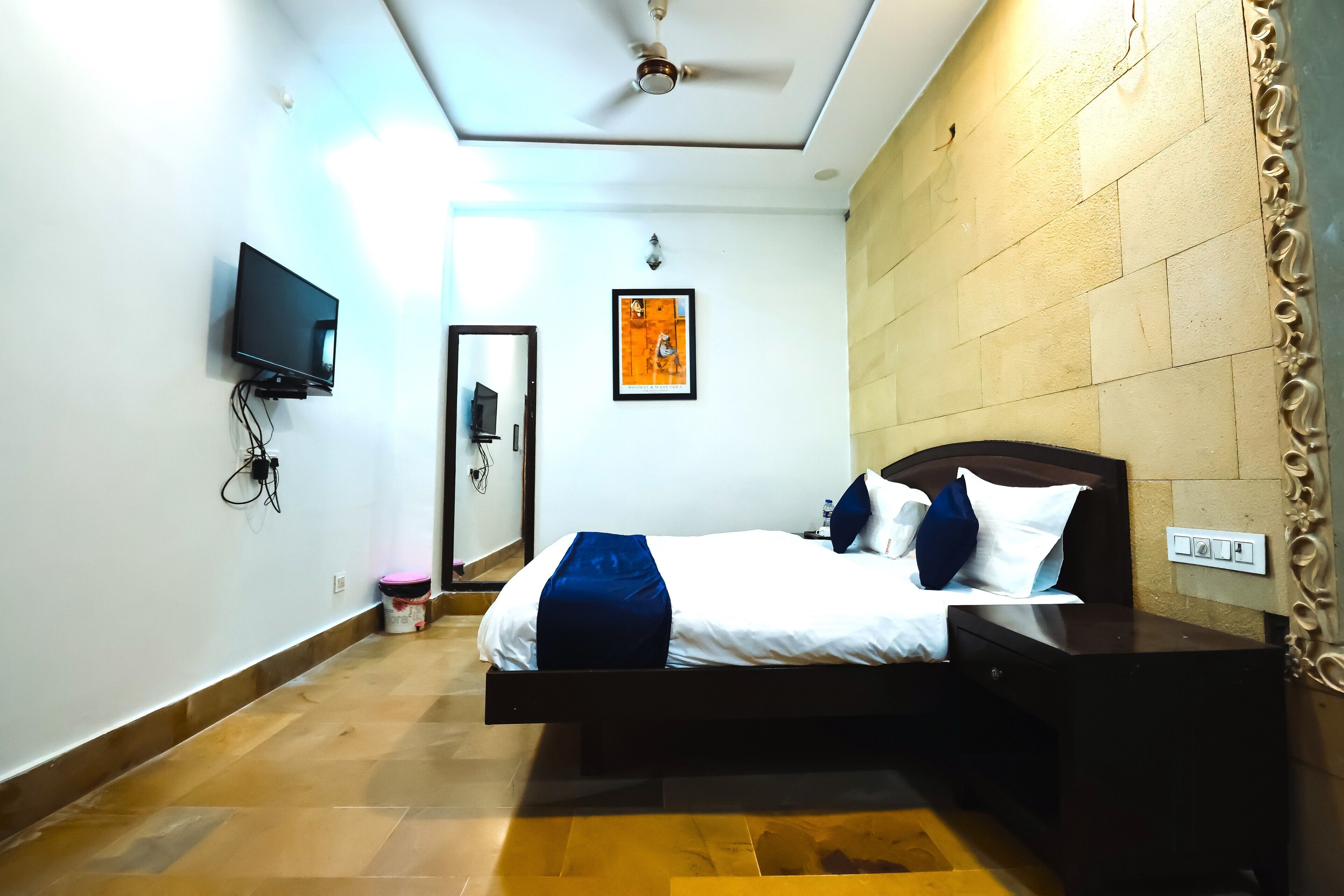 A bedroom with a bed, nightstand, TV, and a wall-mounted light.