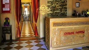 A reception area with a check-in counter, a stone wall with a carved design, and a check-out sign on the wall. - Chirag Haveli - Near Golden Fort (Jaisalmer)