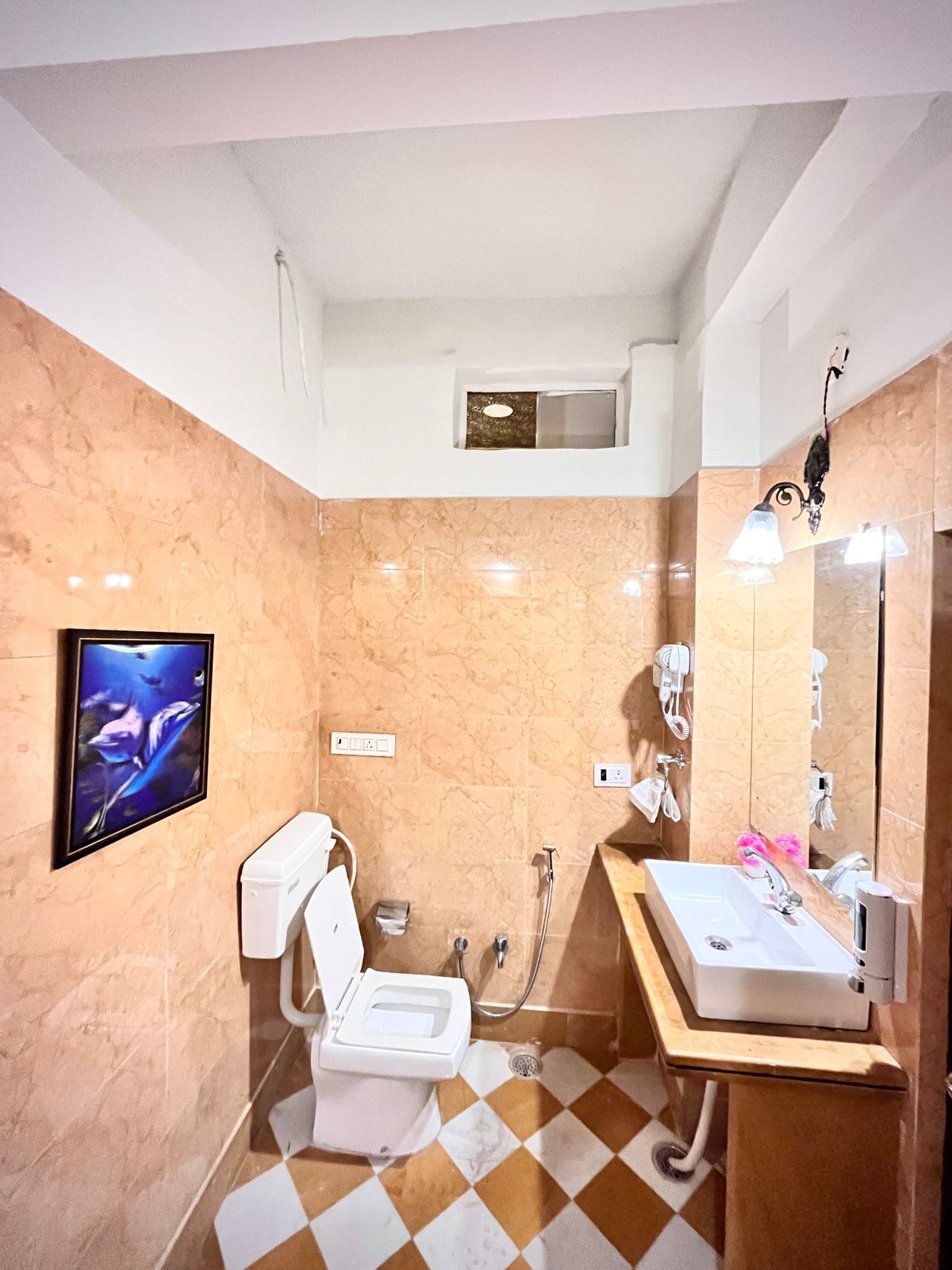 A bathroom with a toilet, sink, and shower. There is a mirror, a towel rack, and a wall-mounted TV.