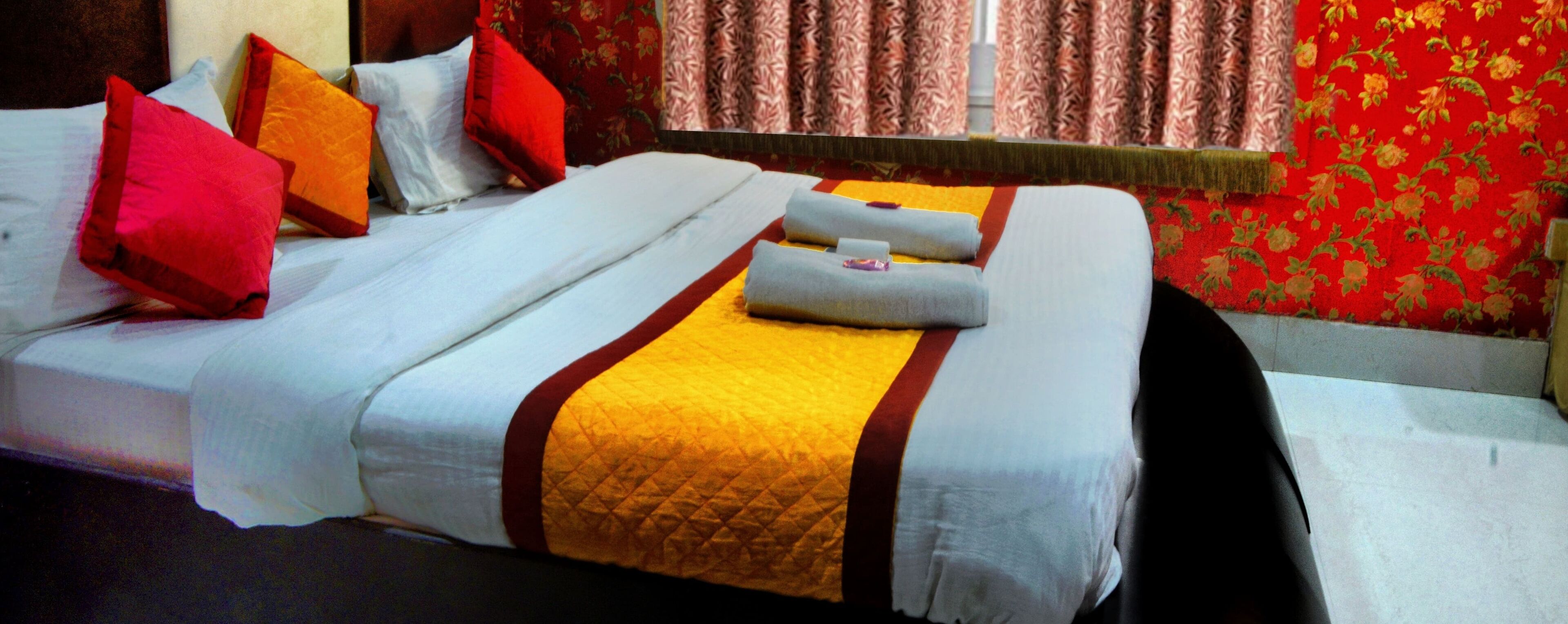 A neatly made bed with white linens, red and yellow pillows, and a quilted blanket.