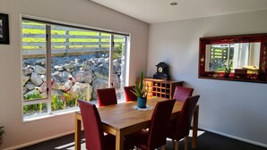 A dining area with a wooden table and red chairs, a clock on the wall, and a view of a stone wall and greenery outside. - Convenient town house close to town and a great location to explore the region (Richmond)