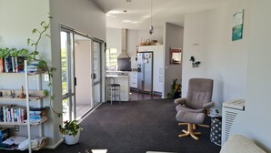 A modern living room with a large window, a bookshelf, a comfortable armchair, and a kitchen area in the background. - Convenient town house close to town and a great location to explore the region (Richmond)