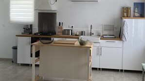 Una cocina moderna con gabinetes blancos, estufa integrada, una lámpara colgante y un ventanal con persianas.