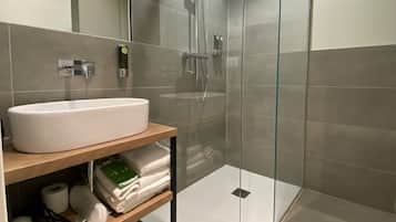 A modern bathroom with a glass-enclosed shower, a white sink, and a shelf with towels and toiletries.
