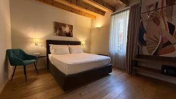 A bedroom with a wooden ceiling, a bed with white linens, a green chair, and a painting on the wall.