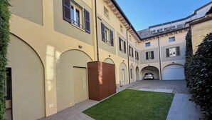 A courtyard with a paved walkway, a small lawn, and a parked car. - Malvezzi24 Boutique Rooms (Desenzano del Garda)