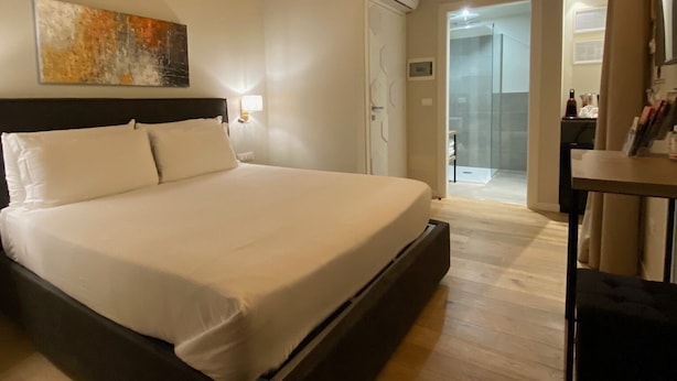 A bedroom with a wooden ceiling, a bed, a bedside table, and a bathroom visible through an open door. - Malvezzi24 Boutique Rooms (Desenzano del Garda)