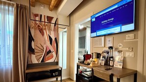 A modern room with a wooden ceiling, a large TV screen displaying a website, a desk with various items, and a bench. - Malvezzi24 Boutique Rooms (Desenzano del Garda)