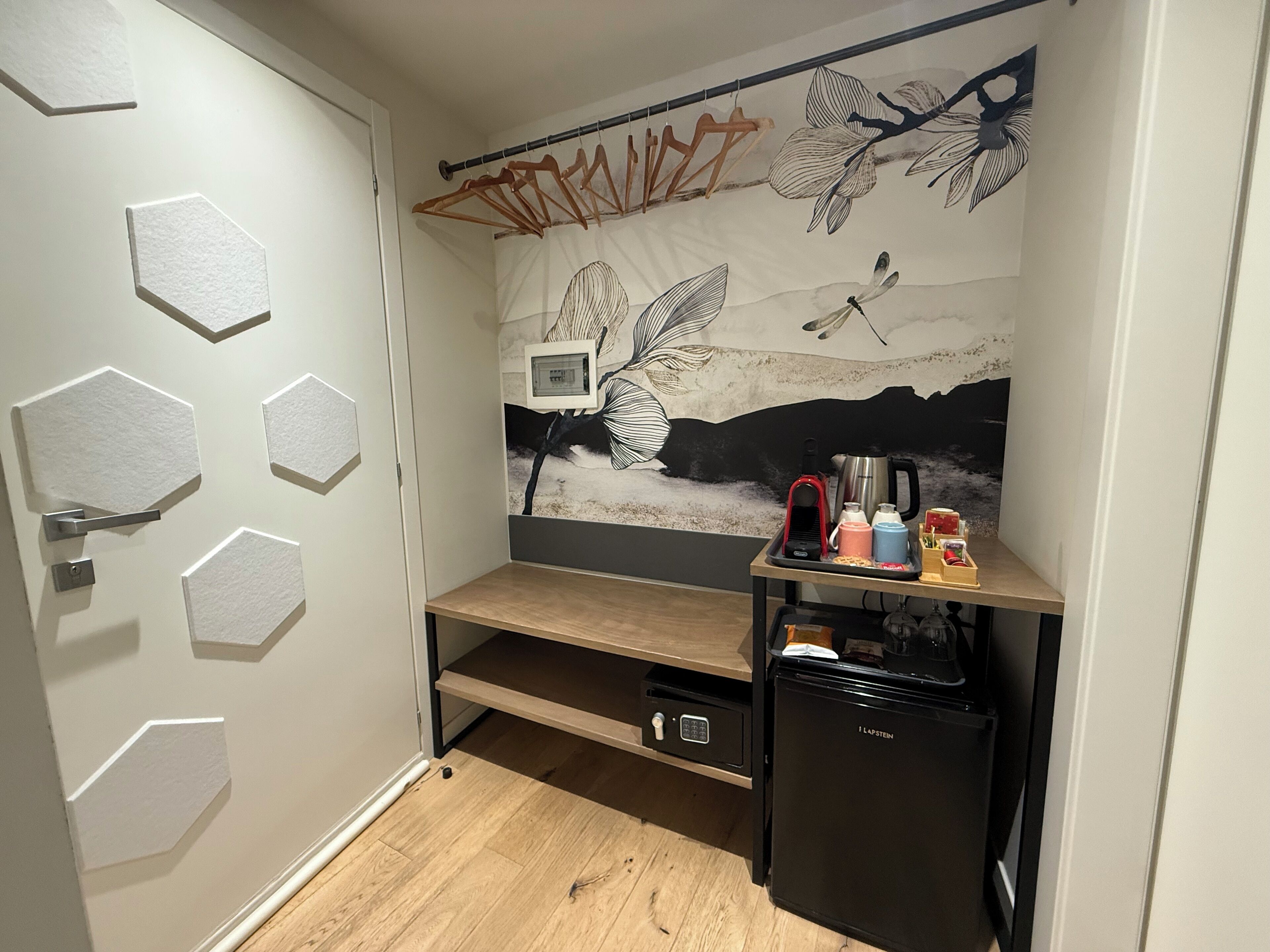 A compact kitchenette with a refrigerator, coffee maker, and a shelf with various items.