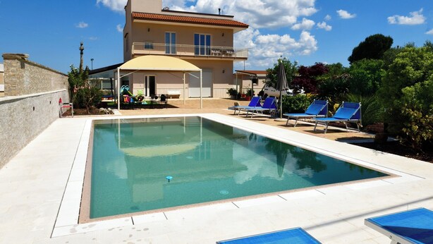 A swimming pool with lounge chairs, a covered patio, and a building with a balcony. - Villa with pool for 8 guests with 3 bedrooms (Puglia)