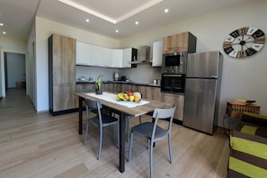 Une cuisine moderne avec une table à manger, des chaises, un panier de fruits et une horloge au mur.