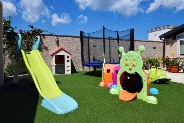 Un espace de jeux pour enfants avec un toboggan, des structures d’escalade et un trampoline.