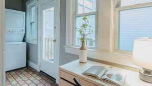 Une buanderie équipée d’un lave-linge et d’un sèche-linge, une porte donnant sur un balcon et une fenêtre avec une plante posée sur le rebord.