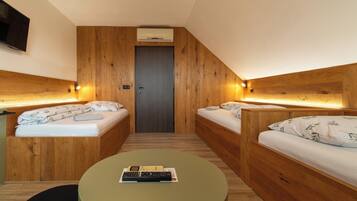 A compact hotel room with two wooden beds, a small table, and a television mounted on the wall.