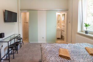 Un dormitorio con cama, escritorio, sillas, televisión y baño visible a través de una puerta abierta.