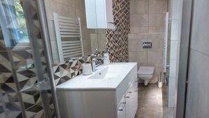 A modern bathroom with a white sink, mirror, and toilet. The walls have a geometric tile pattern, and there is a shower area visible. - Penzion Moon (Ostrava)