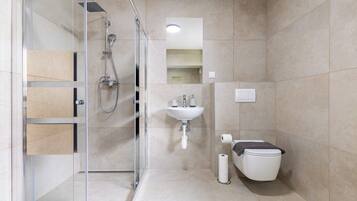 Un baño moderno con cabina de ducha de vidrio, un lavamanos y un inodoro.