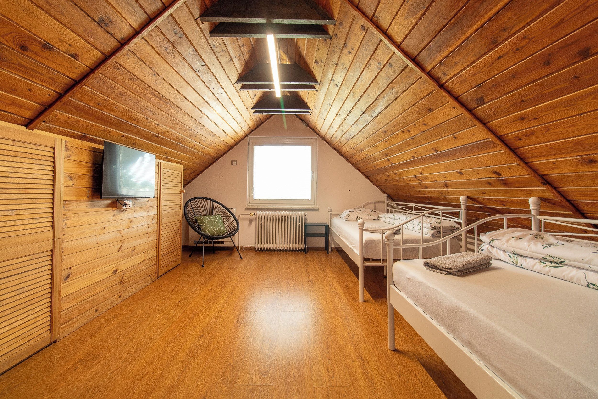 Ein gem ütliches Schlafzimmer im Dachgeschoss mit Holzwänden, einer schrägen Decke, einem Bett, einem Sessel, einem Heizkörper und einem Fernseher.