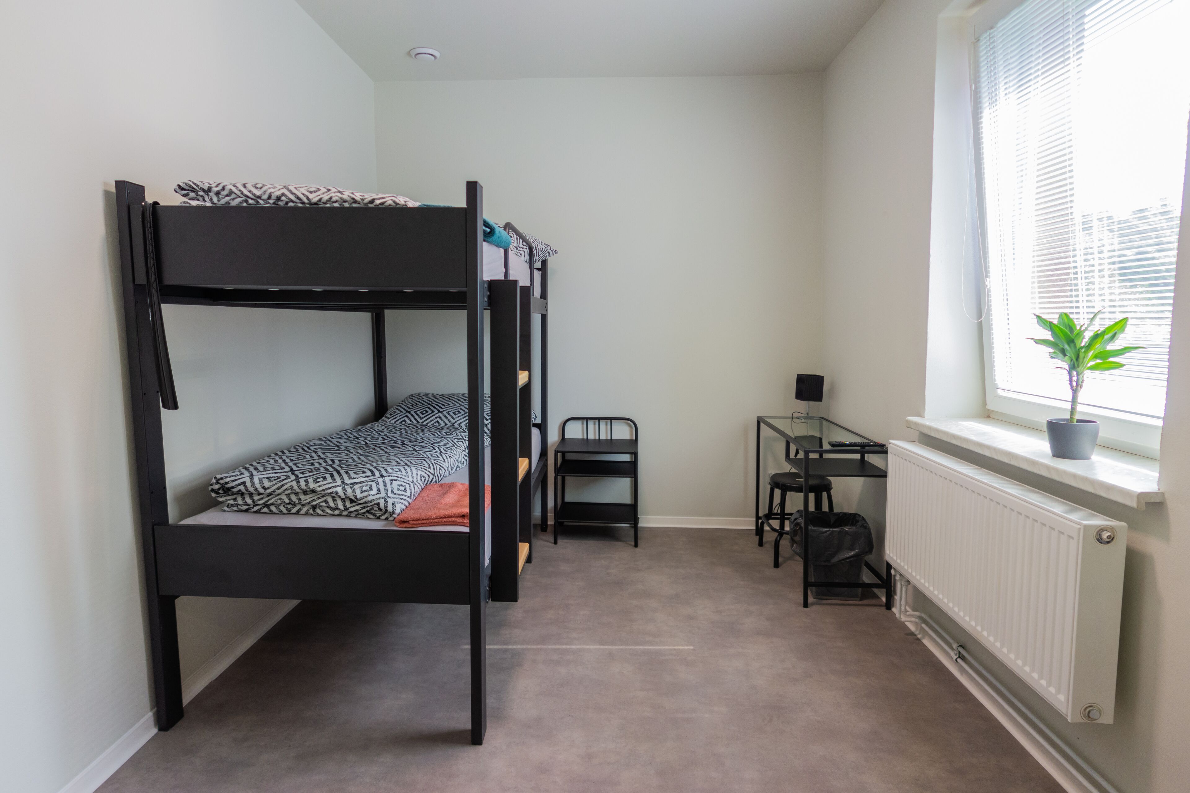 A bunk bed with a desk and chair, a radiator, and a window with blinds.