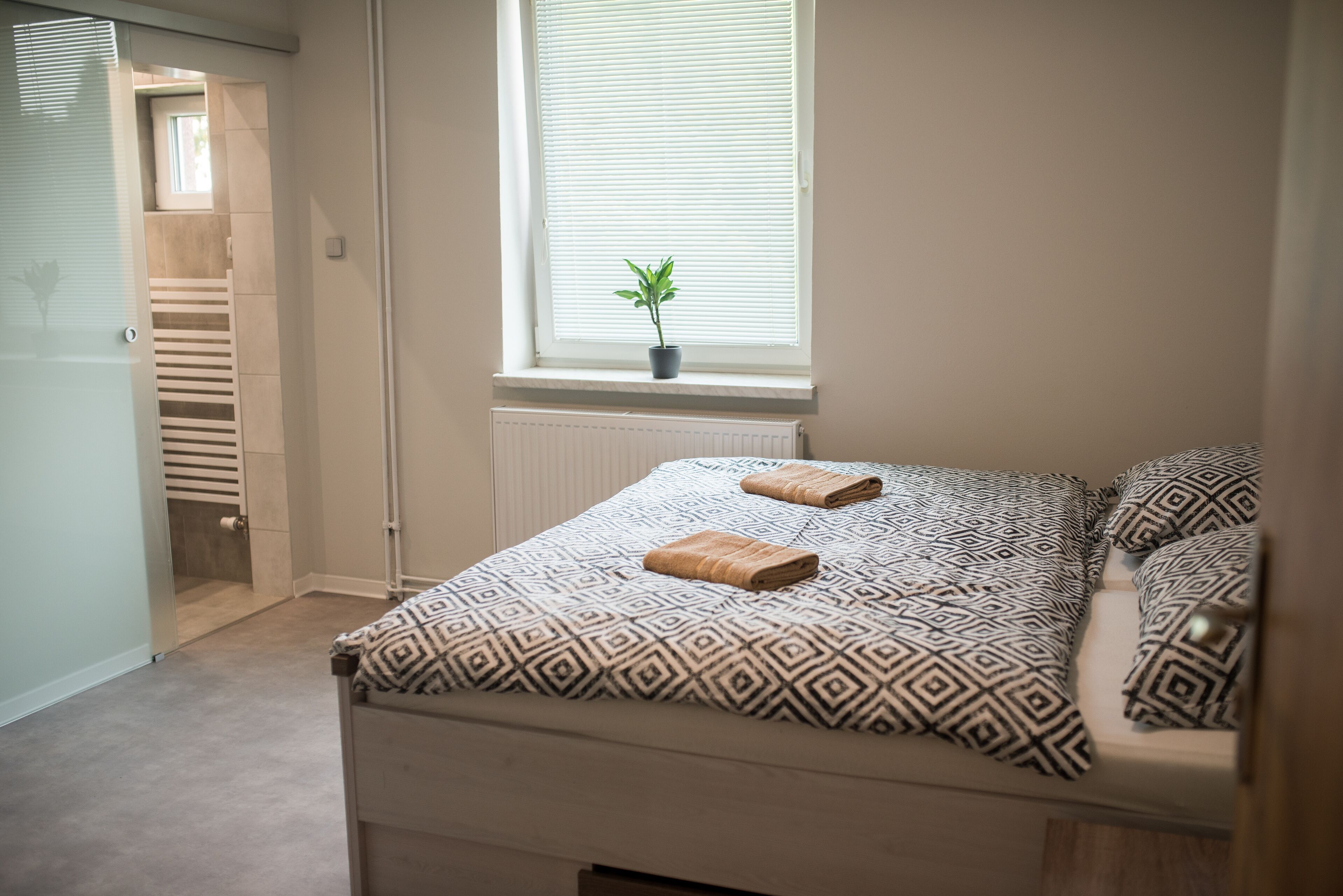 Ein Schlafzimmer mit einem Bett, einer Zimmerpflanze und einem Fenster mit Jalousien.