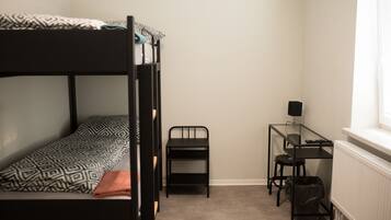 A dormitory room with a bunk bed, a desk, a chair, and a radiator.
