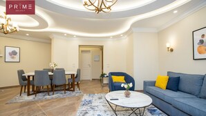 A modern living room with a dining area, featuring a chandelier, a sofa with yellow cushions, and a blue rug. - Prime Select Marvel New Cairo (New Cairo)