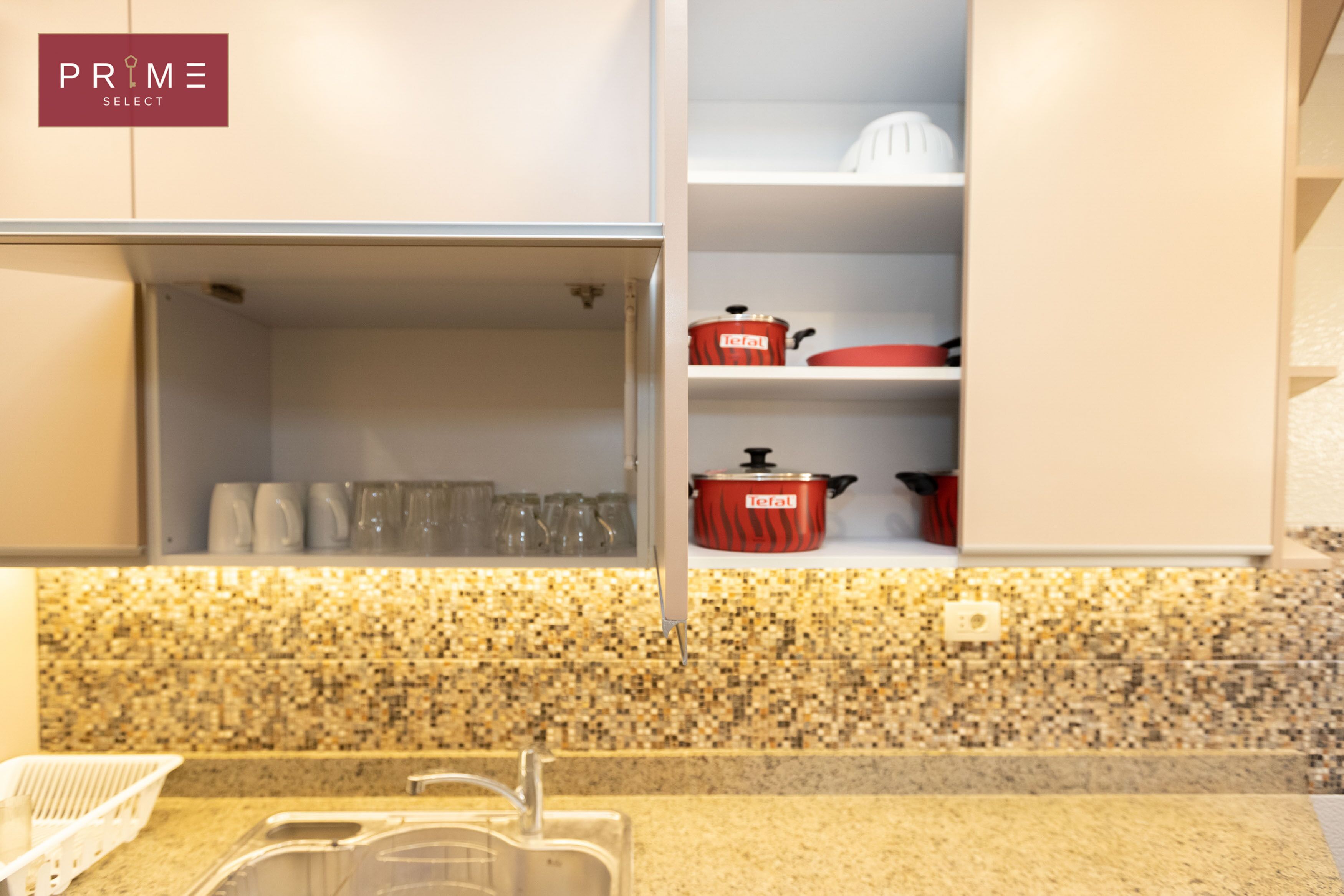 A kitchen with a granite countertop, a sink, and a red pot on the shelf.