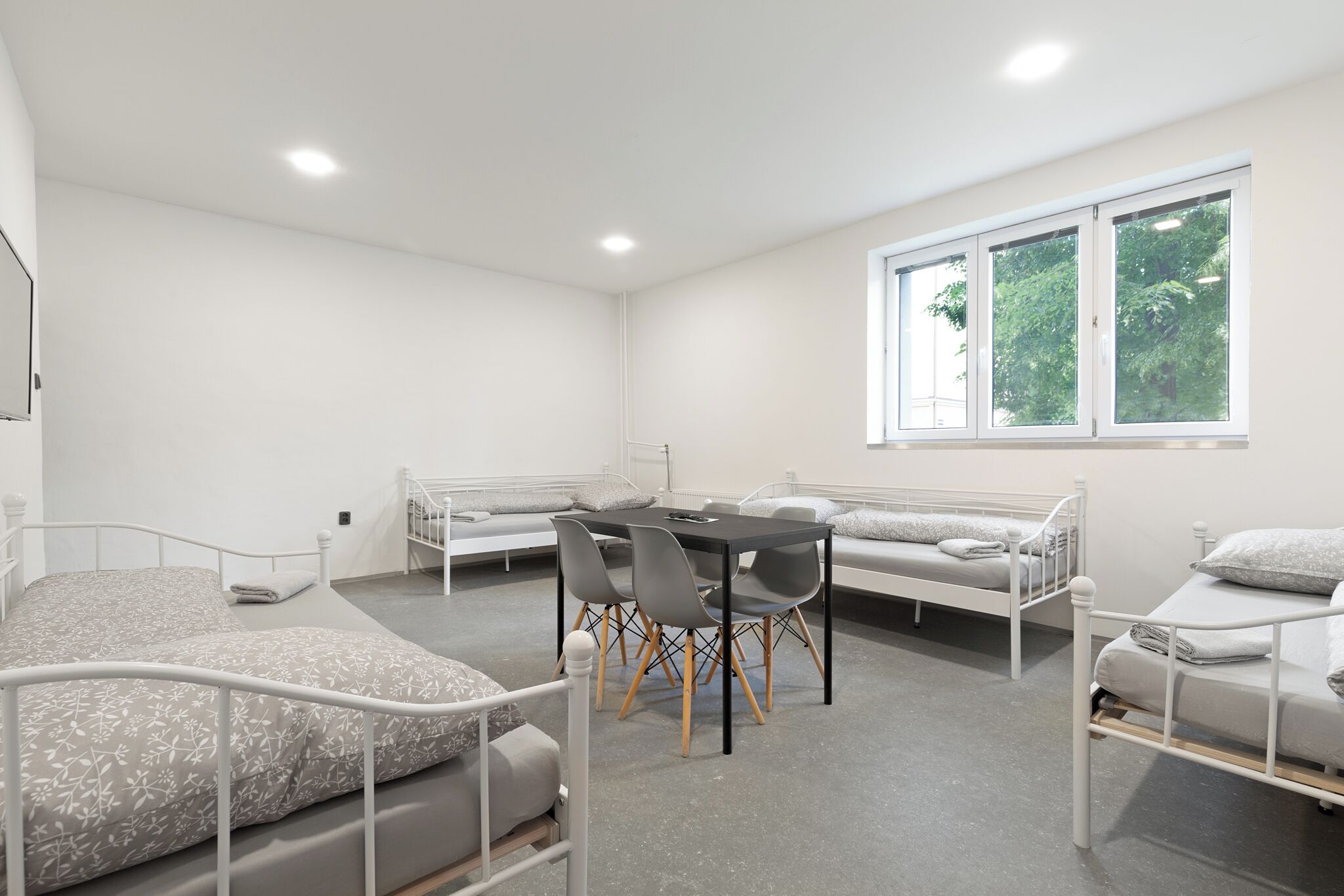 Een kamer met twee bedden, een eettafel met stoelen en een groot raam met uitzicht op bomen.