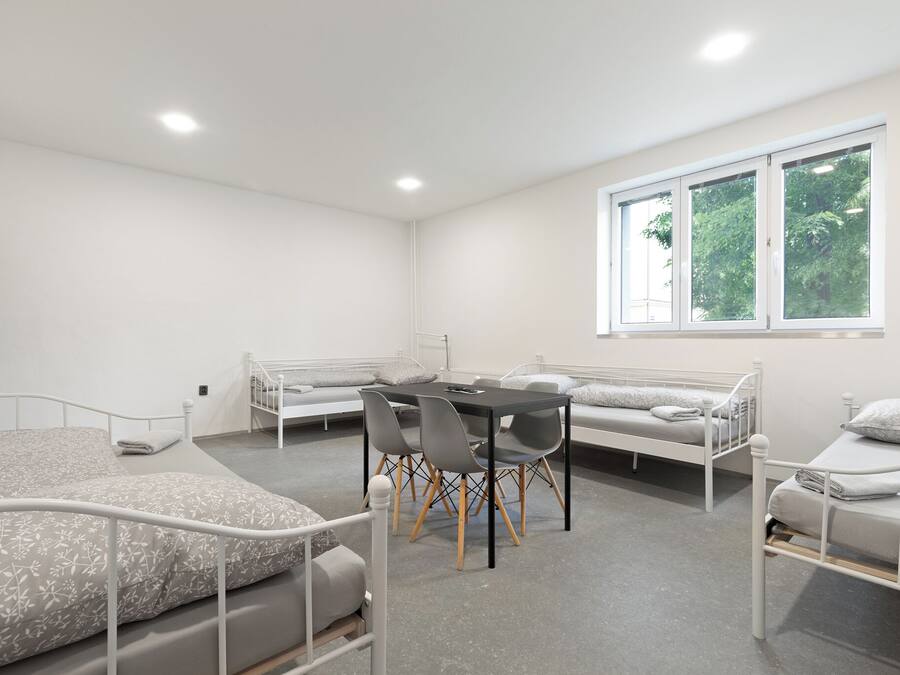 Ein Zimmer mit zwei Betten, einem Esstisch mit Stühlen und einem großen Fenster mit Blick auf Bäume.
