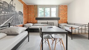 A modern room with a brick wall mural, a large window, a sofa, a dining table, and two chairs. - Hostel na Šalamouně (Ostrava)