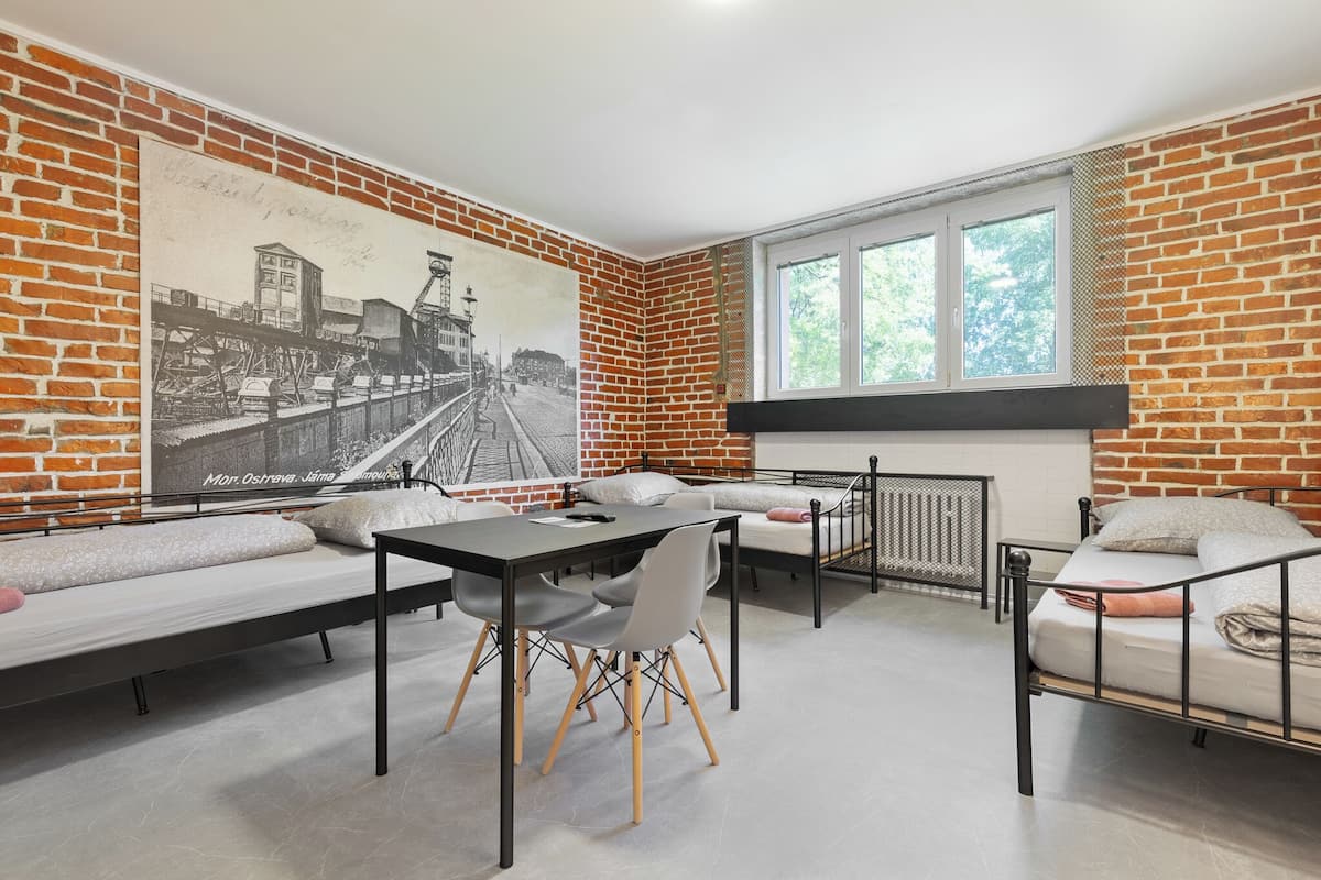 A room with a brick wall, a large black and white photograph, a bed, a desk, and a window.