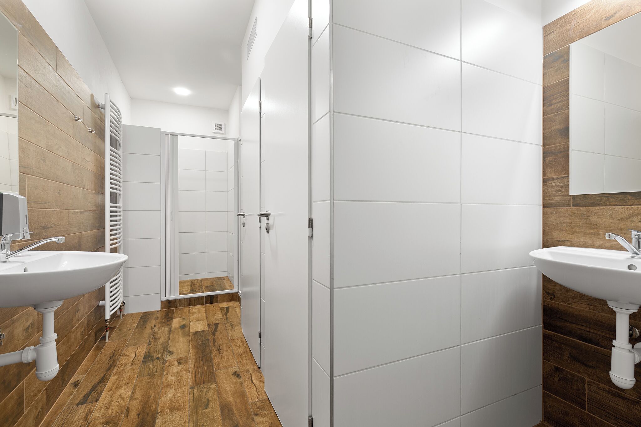 Uma casa de banho moderna com duas pias, soalho em madeira e azulejos brancos.