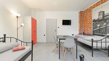 A modern room with a bed, a desk, and a chair. There is a door, a wall-mounted TV, and a brick-patterned wall.
