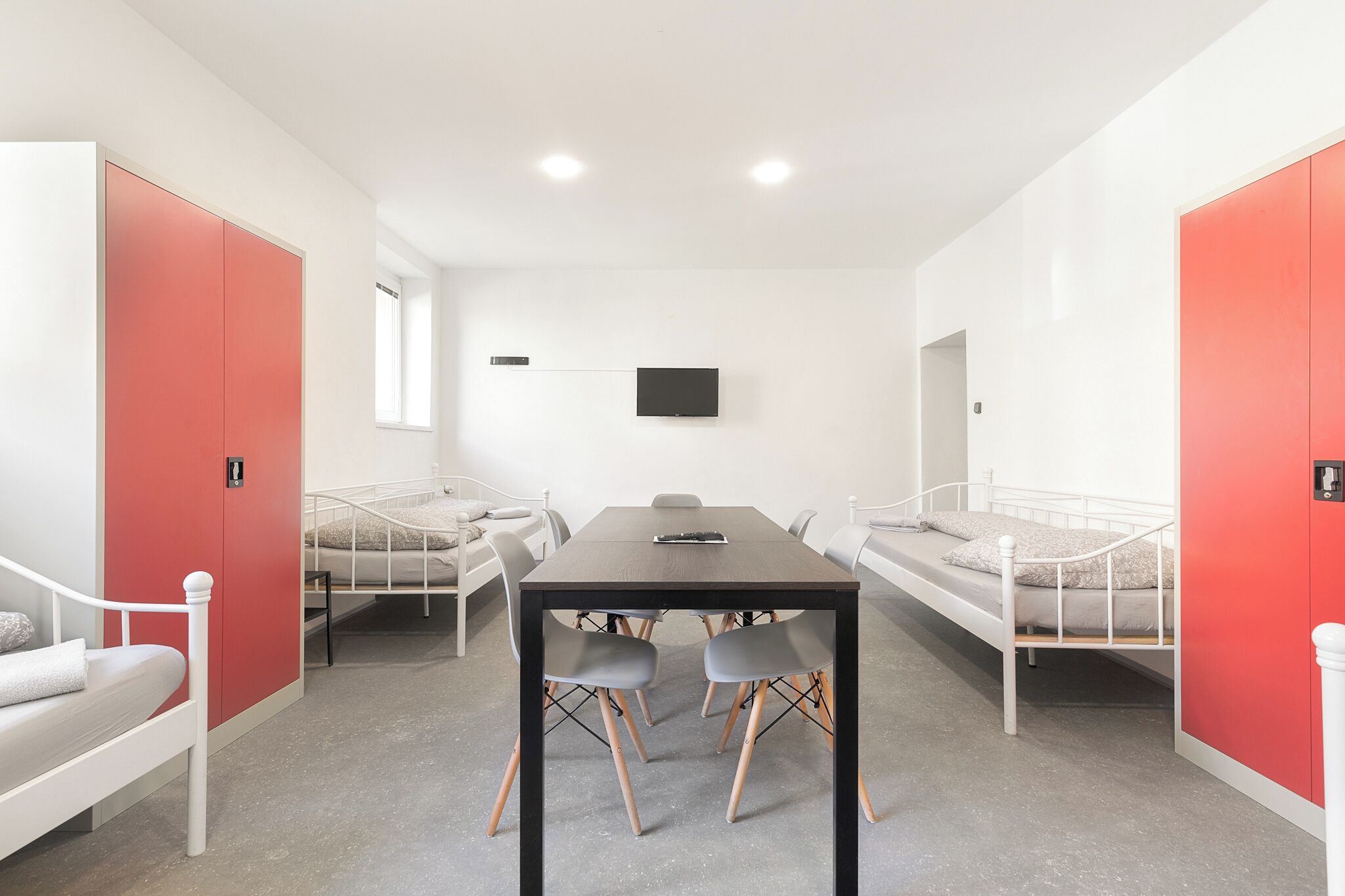 Una habitación moderna con una mesa central, dos camas y un televisor en la pared.