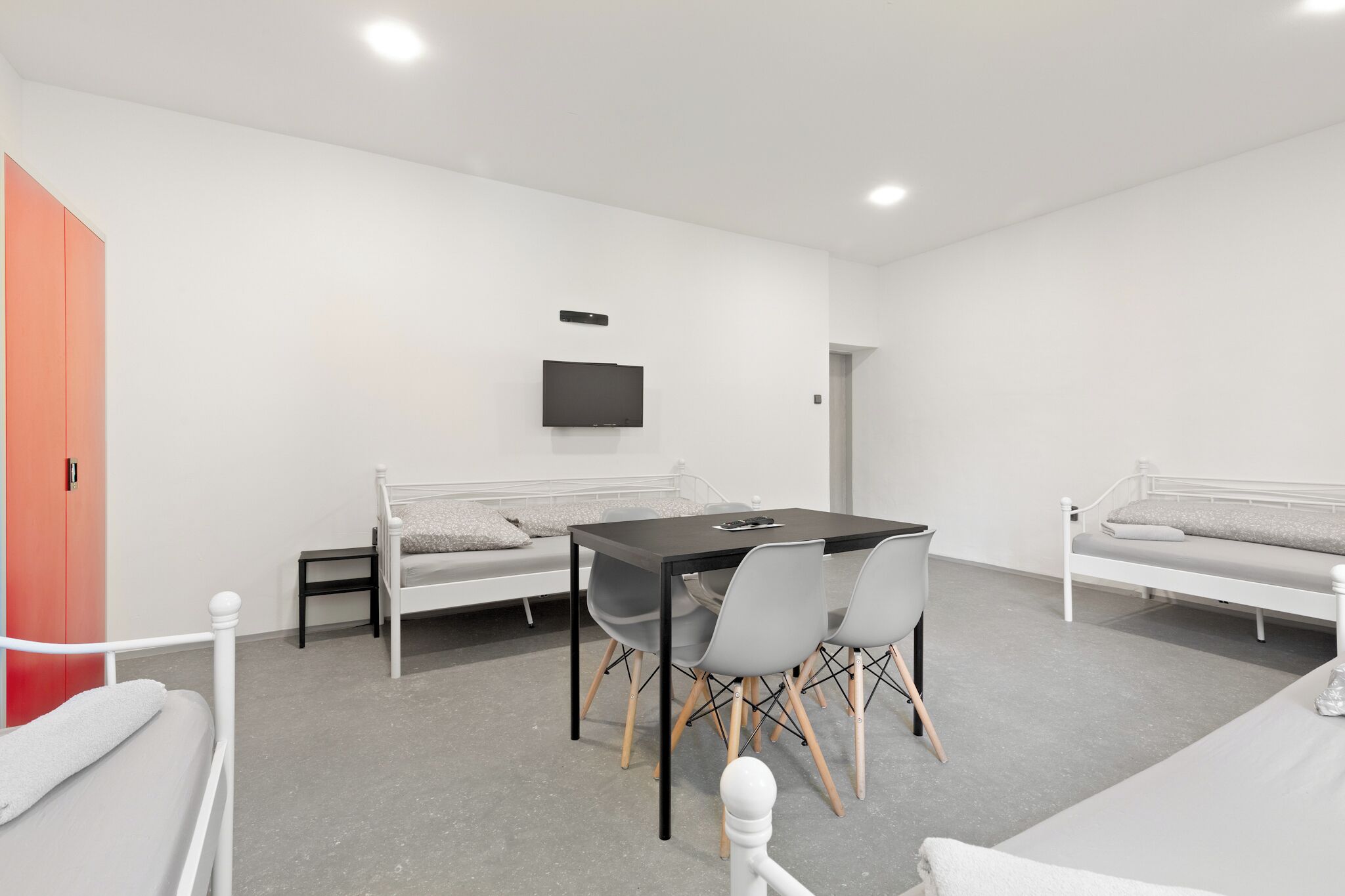 Une chambre moderne avec un lit, une table et des chaises, un téléviseur fixé au mur et une armoire rouge.